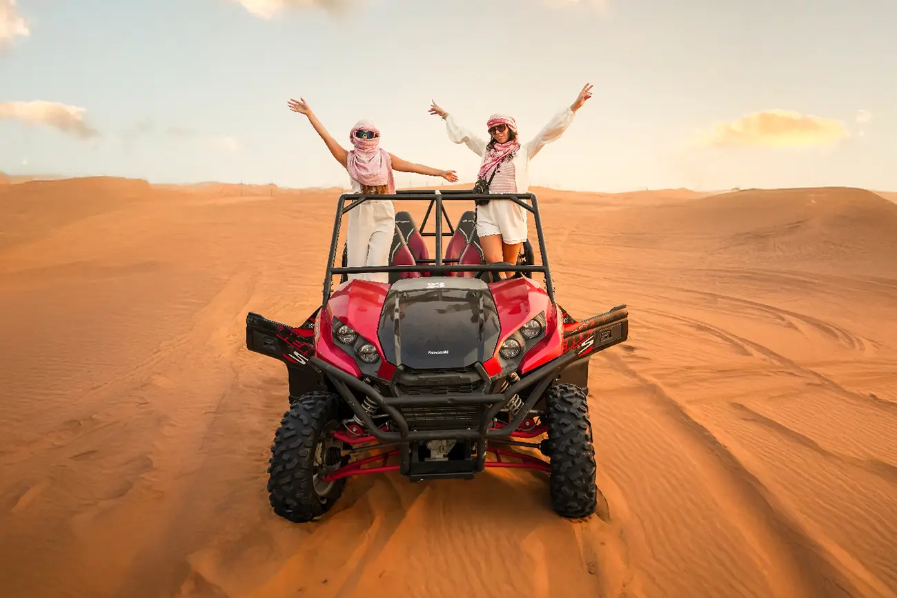 Guests posing with a red Kawasaki buggy on the dunes