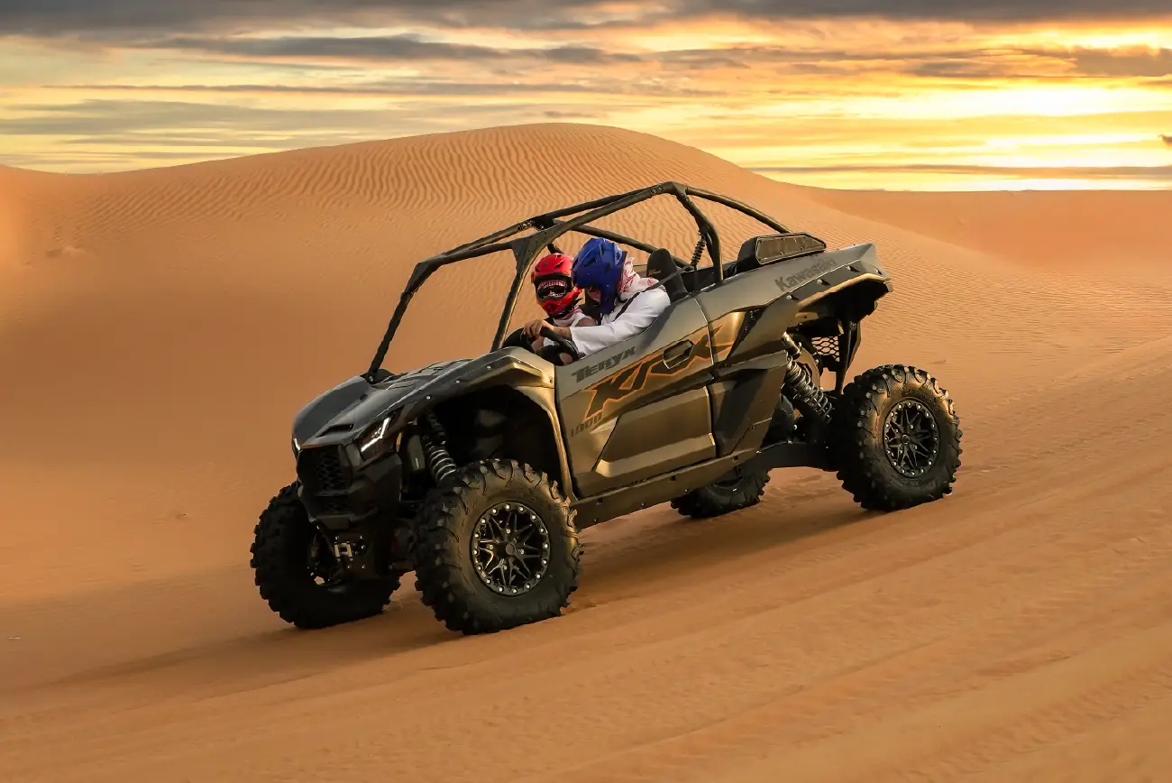 Polaris RZR buggy crossing a dune at sunset
